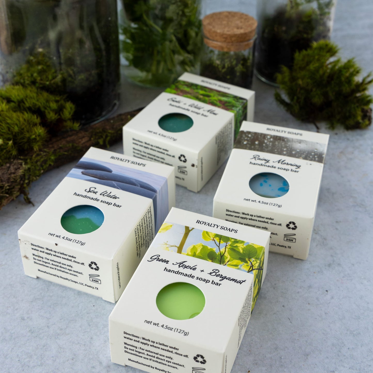 Handmade soap bars in boxes on a textured surface with greenery in the background