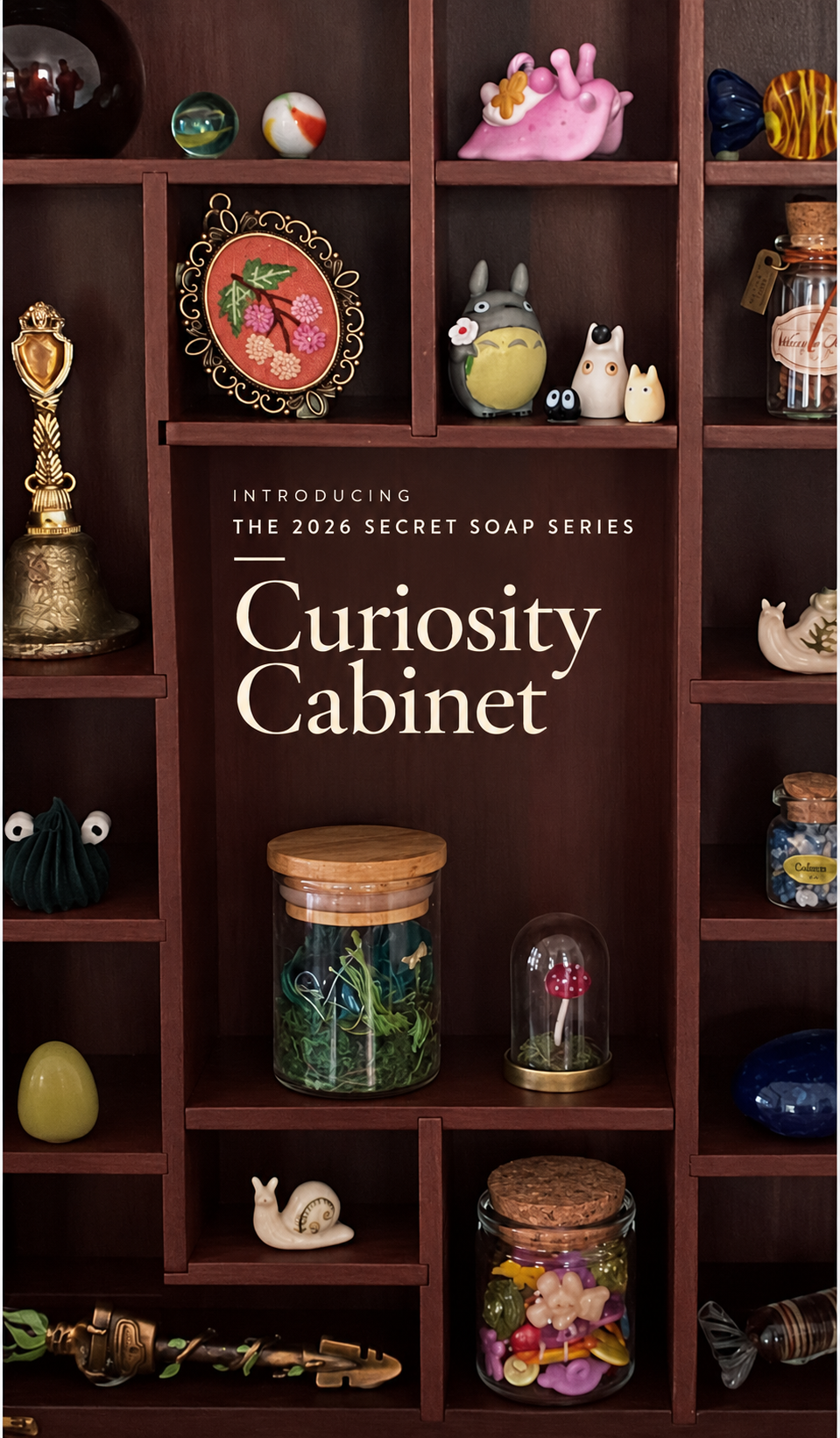 A dark brown wooden shelf filled with assorted decorative objects, including small figurines, glass jars, a framed artwork, and a pink shell, with large centered text reading 'Introducing the 2026 Secret Soap Series Curiosity Cabinet.'.