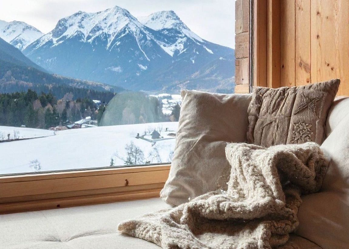 Cozy interior with a sofa and cushions by a window overlooking snow-covered mountains.